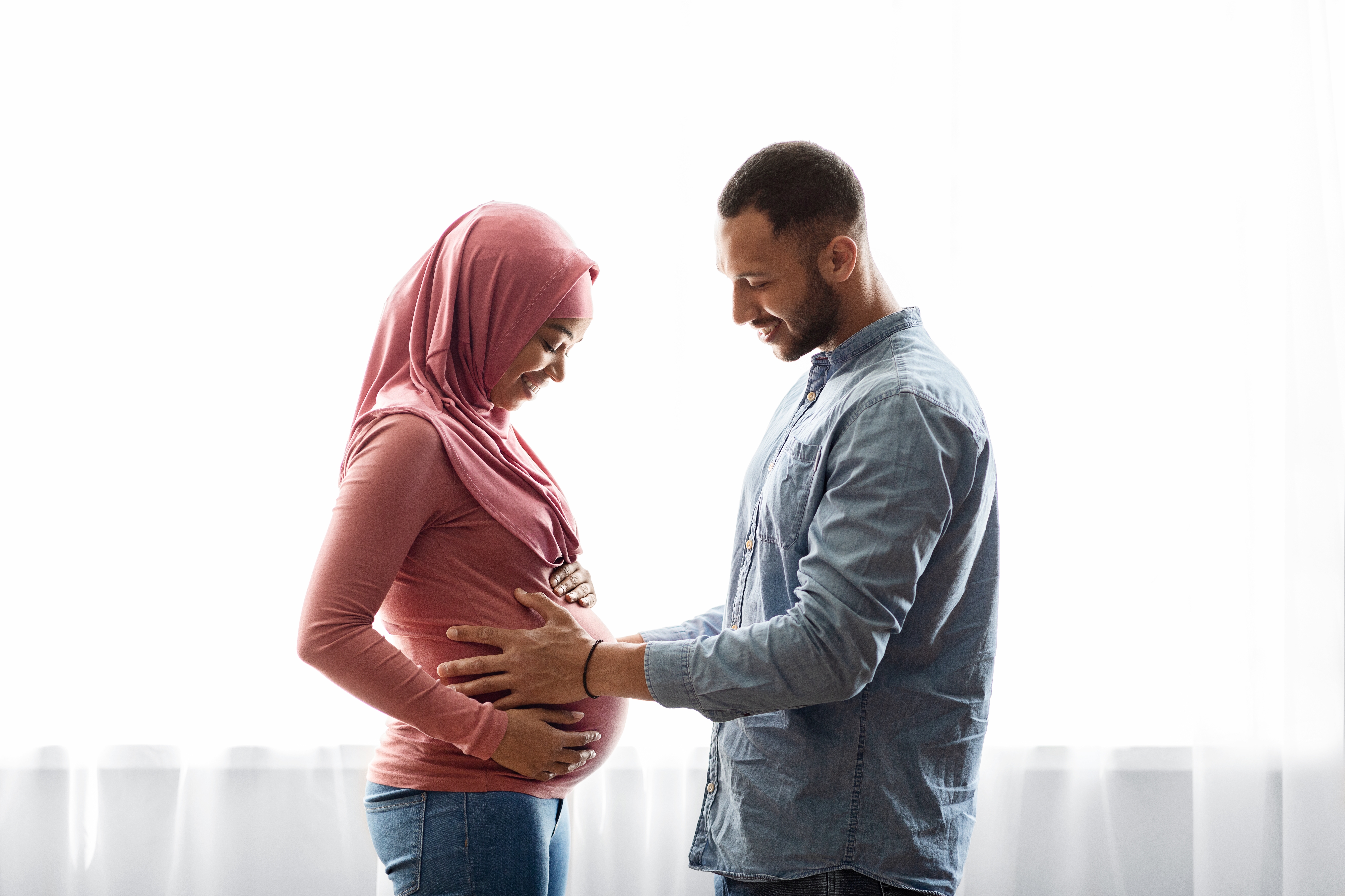 Happy,Black,Pregnant,Islamic,Couple,Standing,Together,Near,Window,At